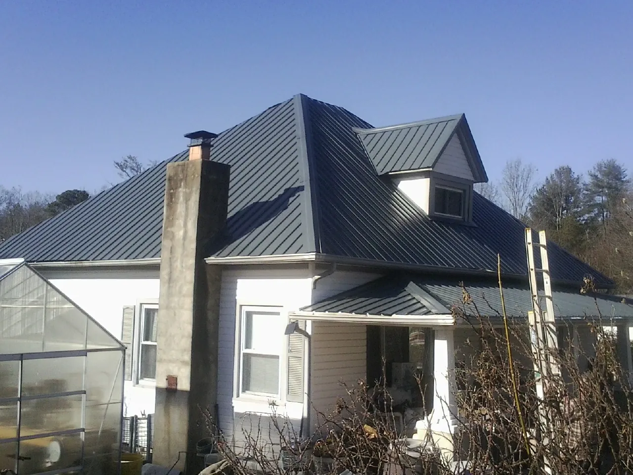 Dark blue standing seam metal roof on a white farmhouse with dormer — Slate & Tile Roof Repair by Roofing Brothers in De Soto