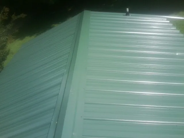 New green metal panels meeting at the ridge of a roof — Flat Roof Repair work by our crew in De Soto
